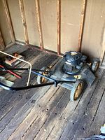 Full side view of lawn mower showing four-wheel design, metal housing, handlebar and engine on top