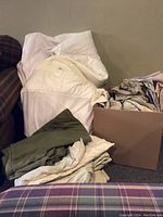Photo showing bag with white mattress pad/comforter and assorted sheets and pillow covers next to a box.