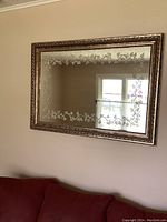 Front view of the rectangular mirror mounted on the wall showing the etched floral border and bronze-tone frame