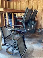 Six metal and mesh patio chairs stacked and arranged in a garage, showing weathered condition and attached swivel chair with built-in metal table.