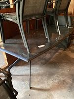 Close-up photo showing the glass top surface of the patio table with visible dirt and dust, along with metal legs visible underneath.