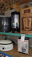 Regal electric coffee maker on shelf next to Nesco roaster oven pot and KitchenAid Chef's Chopper box and white enamel steamer pot.