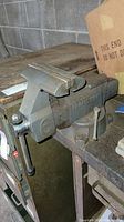 Side view of weathered Craftsman bench vise mounted on workbench with clamp handle visible, showing overall condition and placement.