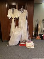 Vintage wedding gown and veil hanging with packaged christening gowns and shoes with clutch on floor.
