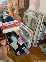 Photo showing Baby Bjorn rocker, three folded white baby gates stacked, boxed Jolly Jumper, Ikea Antilop high chair, and three baby pyjamas/onesies placed on rocker.