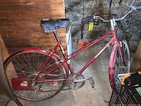 Side view of red Raleigh bicycle showing frame, saddle, wheels, and drivetrain in basement setting.
