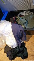Clothing items in a bin including white skirt or garment, green garment bag, and navy blue and black clothing pieces.