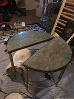 Pair of demilune metal framed end tables with faux marble tops shown side by side on a carpeted floor with surrounding household items.