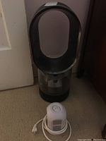 Dyson bladeless fan standing next to white extension cord on carpet, showing overall view of items.