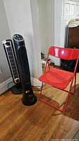 Image shows two tower fans and one red folding chair in a room corner.