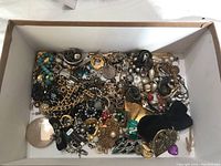 Box filled with a large quantity of assorted costume jewelry including bracelets, necklaces, rings, and brooches of varied colors and materials.