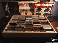 Photo of Beatles and Bruce Springsteen LP albums with wooden rack filled with assorted music cassettes.
