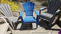 Photo showing four plastic Muskoka style chairs outdoors on stone patio, three brown and one blue.