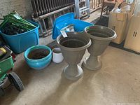 Wide view showing all four pots together in a garage setting, two large plastic pedestal pots, turquoise and white ceramics visible