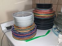 Two stacks of kitchen plates on counter, colorful and white plates visible, some with chips.