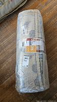 Rug rolled and wrapped in plastic showing lot tag and part of label.