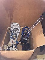 Box containing two pairs of snowshoes, boots, tennis rackets, and hiking poles.