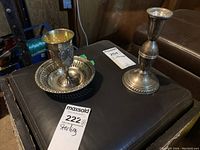 Candlestick, bowl and goblet displayed together on black surface with inventory tag