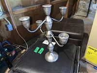 Sterling silver five-arm candelabra placed on a black cushioned stool in a basement. Shows tarnished surface indicating need for cleaning.