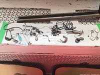 Wide view of sterling silver necklaces and earrings laid on a white surface with pink background. Items include necklaces with different pendants like blue stone and heart shapes, and several pairs of earrings in various styles.