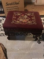Full view of the stool showing maroon embroidered top and carved wooden legs