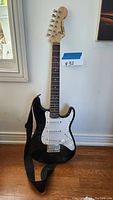 Full front view of the Fender Squier Mini Stratocaster electric guitar showing black body, white pickguard, maple neck, rosewood fretboard, and black strap attached