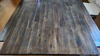 Close-up top view of large dark wood dining table surface showing wood grain, distressed finish, and signs of wear.