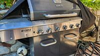 Close-up of the Nexgrill Deluxe propane grill front with six control knobs and two cabinet doors below.
