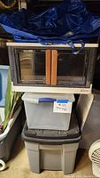 Three storage containers stacked and two blue IKEA bags on top