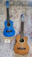 Top view of two acoustic guitars side by side on carpet: light brown Espanola and blue Lauren guitar.