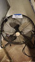 Black Utilitech floor fan with a wire cage and three blades on a floor.