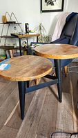 Side view showing the round wooden tabletop with natural wood grain and three black tapered legs.