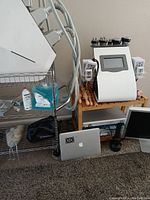 Photo showing G5 Ultra Slimming machine with massage heads on wooden stand, ultrasonic gel gallon, steel cart with supplies, laptop and monitor on floor
