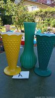 Three decorative vases on a table outdoors, two green hobnail and one yellow hobnail vase