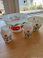 Four piece set on countertop near window: large apple design mixing bowl, medium tulip design mixing bowl, and two small tulip design storage jars.