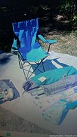 Photo of blue adult folding chair and camping accessories on mat outdoors in daylight