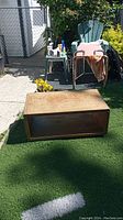 Vintage all wood coffee table placed on artificial grass outside, showing front and top surfaces with visible wear.