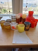 Full view of all mugs, glasses, and the red pitcher arranged on a wooden table.