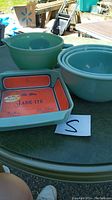 Three nested round Jade-ite mixing bowls, separate large round Jade-ite batter bowl and square casserole dish on outdoor table