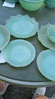 Six pieces of pale green jadeite glassware on table, 4 plates and 2 bowls, showing different embossed patterns and scalloped edges.