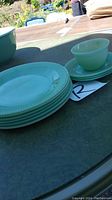 Stack of 6 jadeite plates, 3 saucers, and single cup on top, all in mint green color with ribbed edges on plates and saucers.