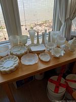 Overview of milk glass collection including divided plates, vases, bowls, and dishes on a wooden table by window light.