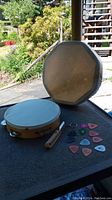 Photo showing the indigenous octagonal frame drum, wooden tambourine, whistle and guitar picks laid out on a table outdoors
