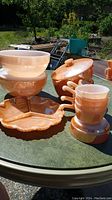 Photo showing all the peach luster bowls, divided plate, and lids outdoors in sunlight on table.