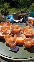 Wide view showing multiple pieces of peach luster swirl glass including bowls, cups, creamer, and sugar bowl on a glass table outdoors.