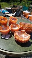 Multiple peach luster glass bowls arranged on a round table under natural light. Includes various bowl shapes: round, shell-shaped, and bubble styles.