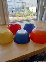 Set of five vintage Pyrex mixing bowls in various sizes and primary colors placed upside down on wooden surface by a window
