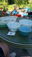 Outdoor photo of all items arranged on a round table, showing 3 Pyrex bowls and 2 casserole dishes with glass lid.