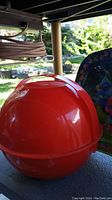 Closed red spherical picnic ball container photographed outdoors showing its bright red plastic surface and glossy finish.