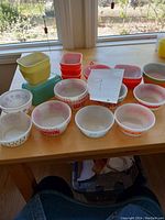 Photo of various small bowls with different vintage patterns, white glass with red, pink, yellow, brown designs, and red and yellow square pyrex containers with lids stacked beside the bowls.